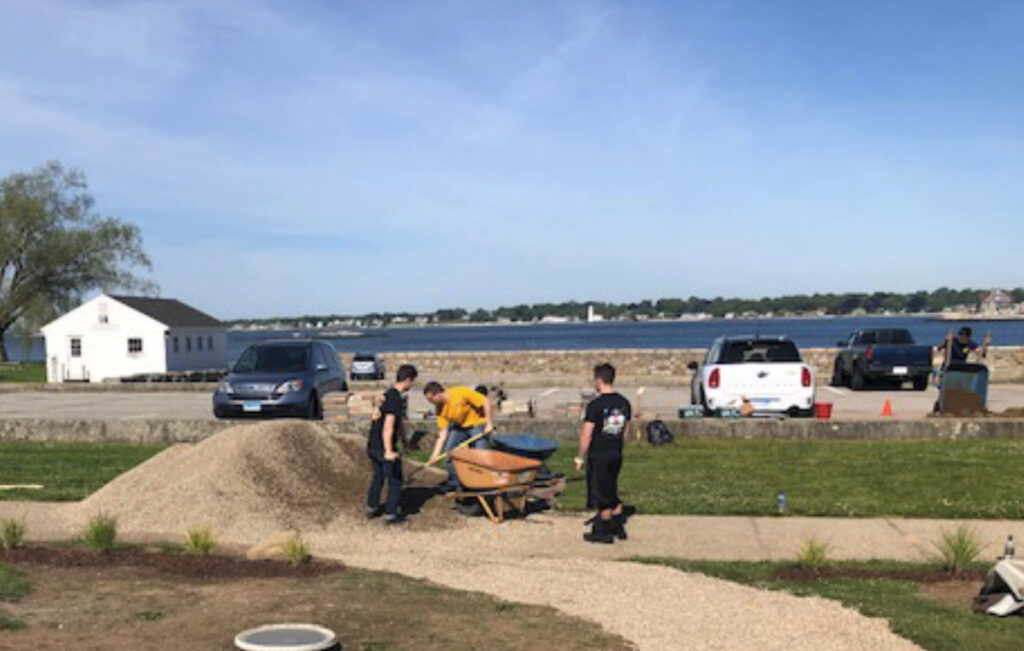 Workers place gravel on the fabric and will compact.