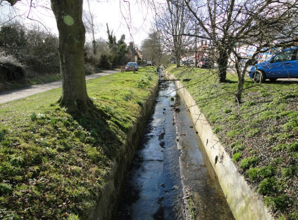 An aging stormwater infrastructure running alongside a road, showing signs of wear.